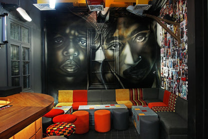 A room with a large canvas artwork featuring a person's face, with a mix of furniture including bean bags and ottomans in an L-shaped arrangement, in a setting that resembles a home interior.